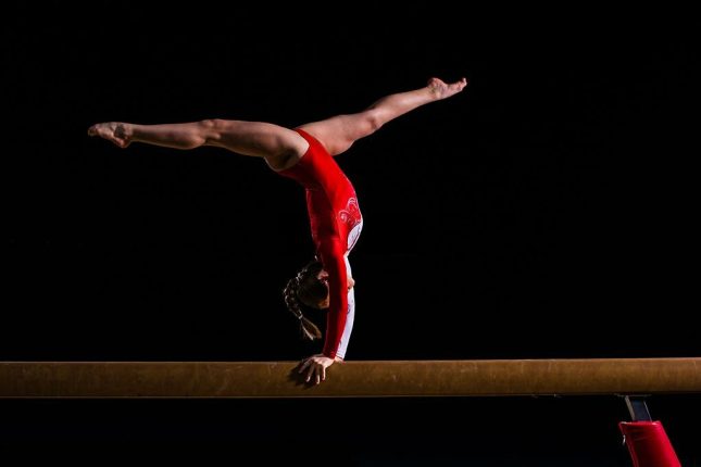 Young woman balancing on balance beam in sports hall.