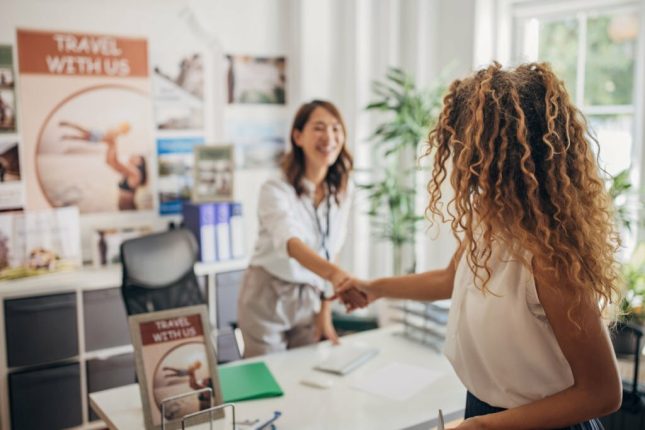 Two people, a beautiful woman arrive at a modern travel agency and shake hands with the travel agent.